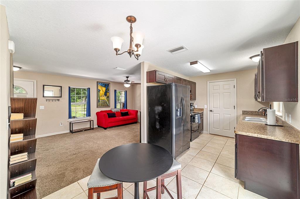 A kitchen with dark cabinets and a dining area opens into a carpeted living room — 2854 SE 140TH LANE, SUMMERFIELD, FL