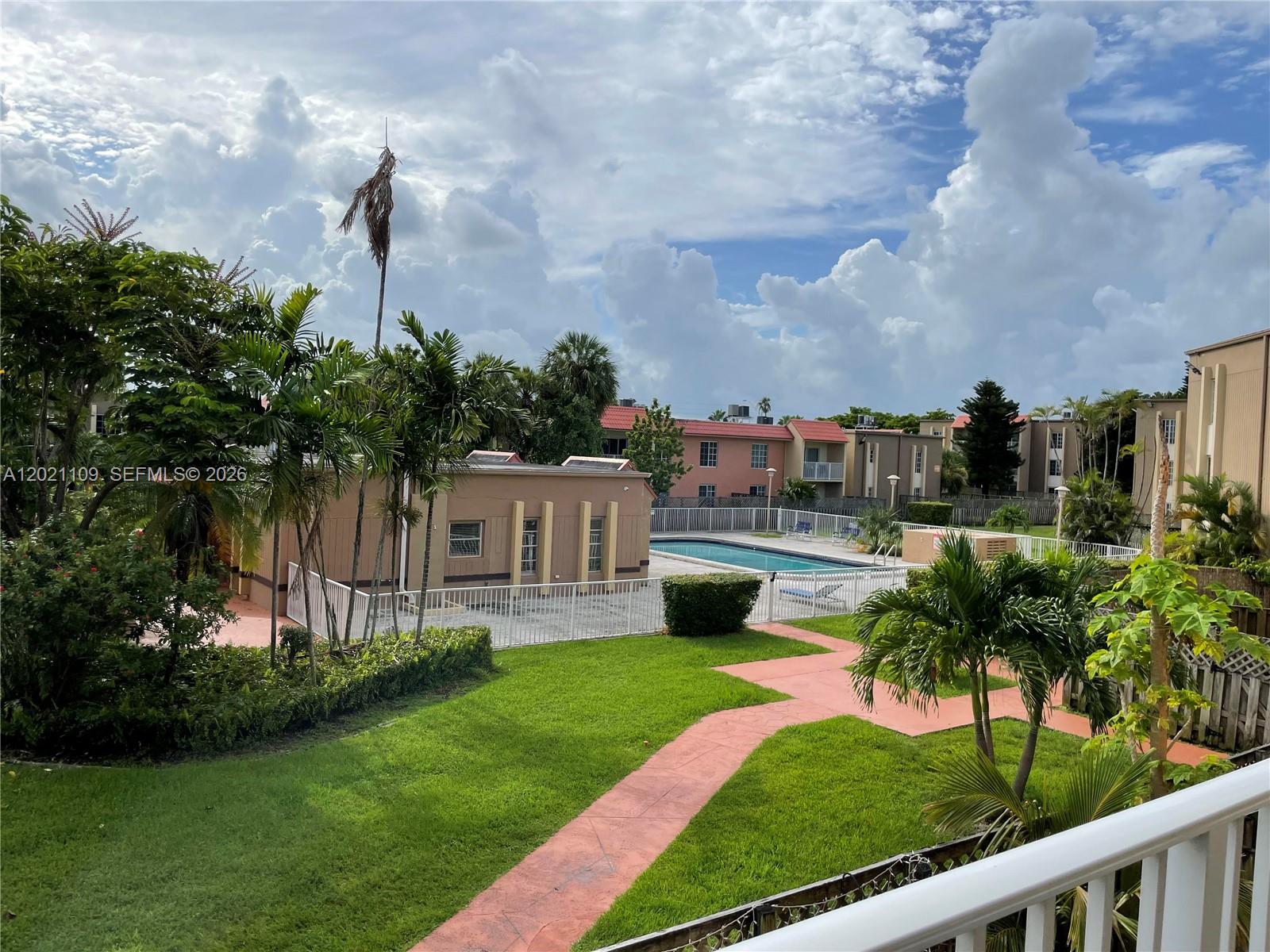 An outdoor view shows a swimming pool, a small building, and palm trees on a lawn — 4920 NW 79th Ave # 212, Doral FL 33166, DORAL, FL