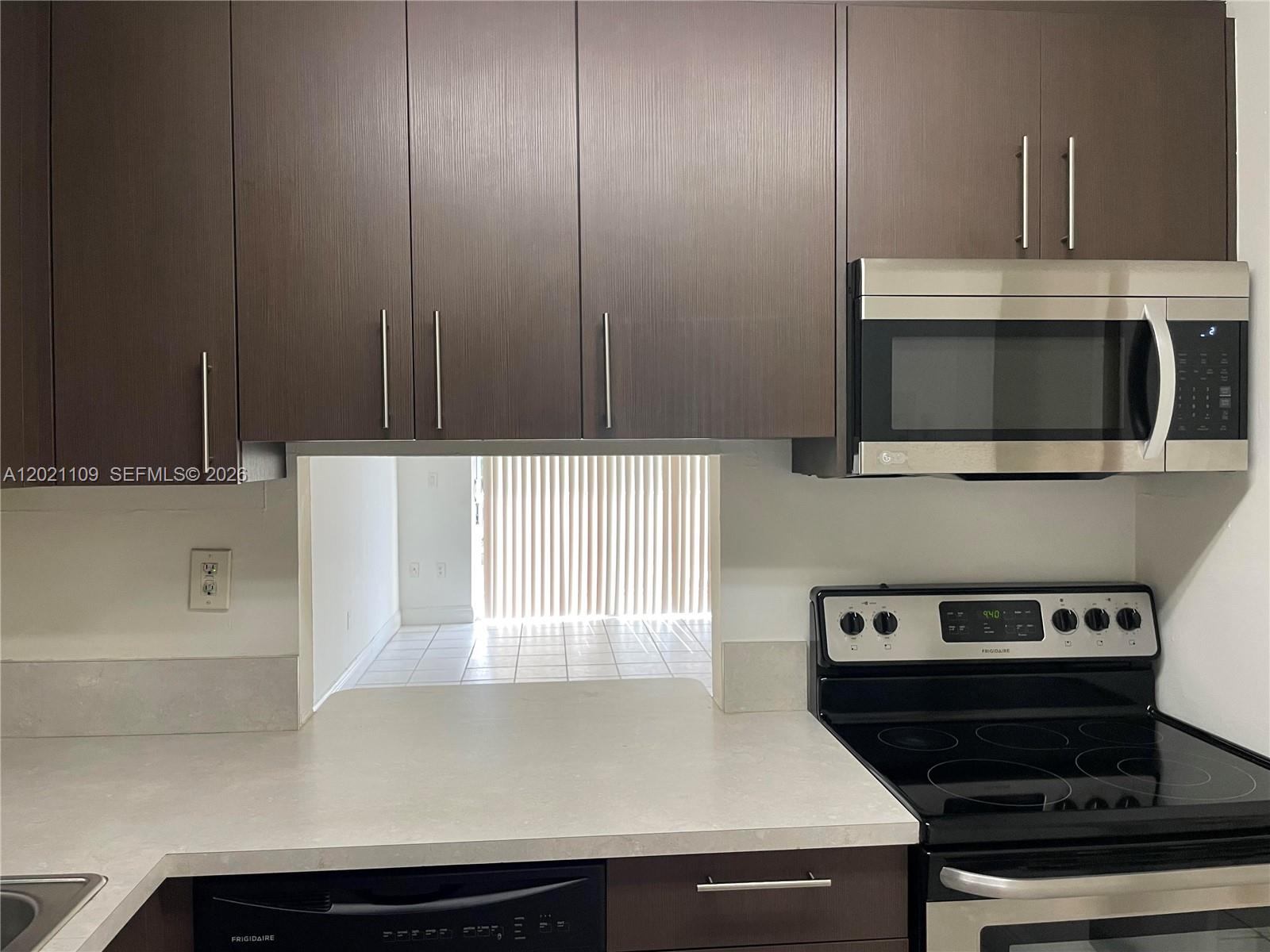 A kitchen features dark wood cabinets, stainless steel appliances, and a pass-through window — 4920 NW 79th Ave # 212, Doral FL 33166, DORAL, FL