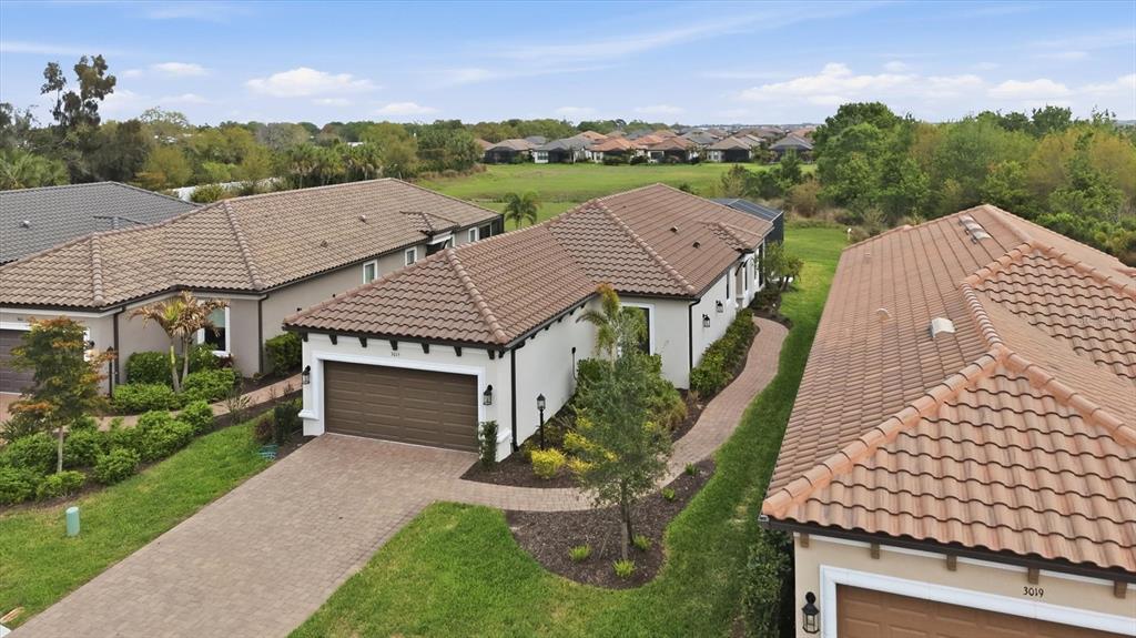 An aerial view shows two suburban houses with brown tile roofs and paved driveways — 3015 TOLMINO COURT, BRADENTON, FL