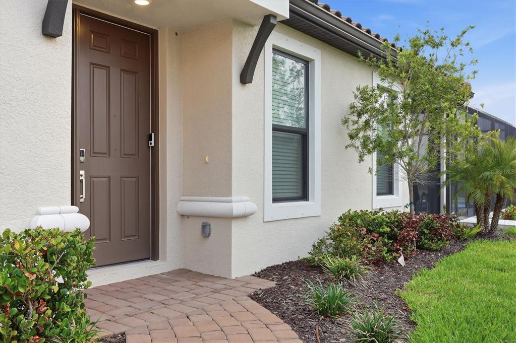 A brown front door with a keypad lock sits beside a window on a stucco house — 3015 TOLMINO COURT, BRADENTON, FL