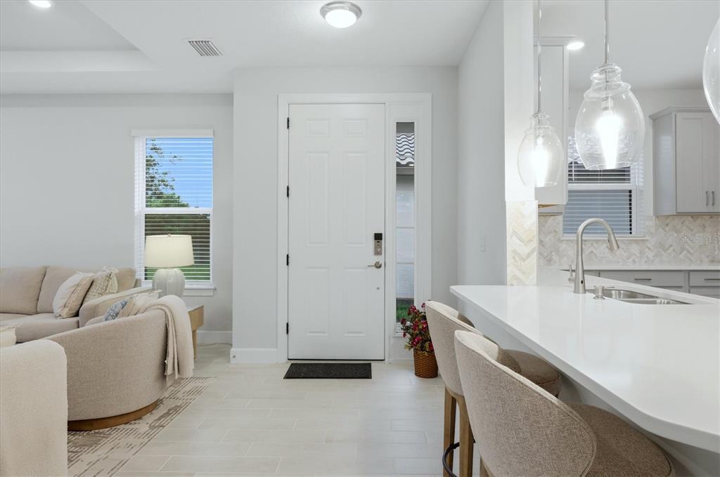 A bright, open-concept kitchen and living area features white cabinetry, quartz countertops, and tile flooring — 3015 TOLMINO COURT, BRADENTON, FL