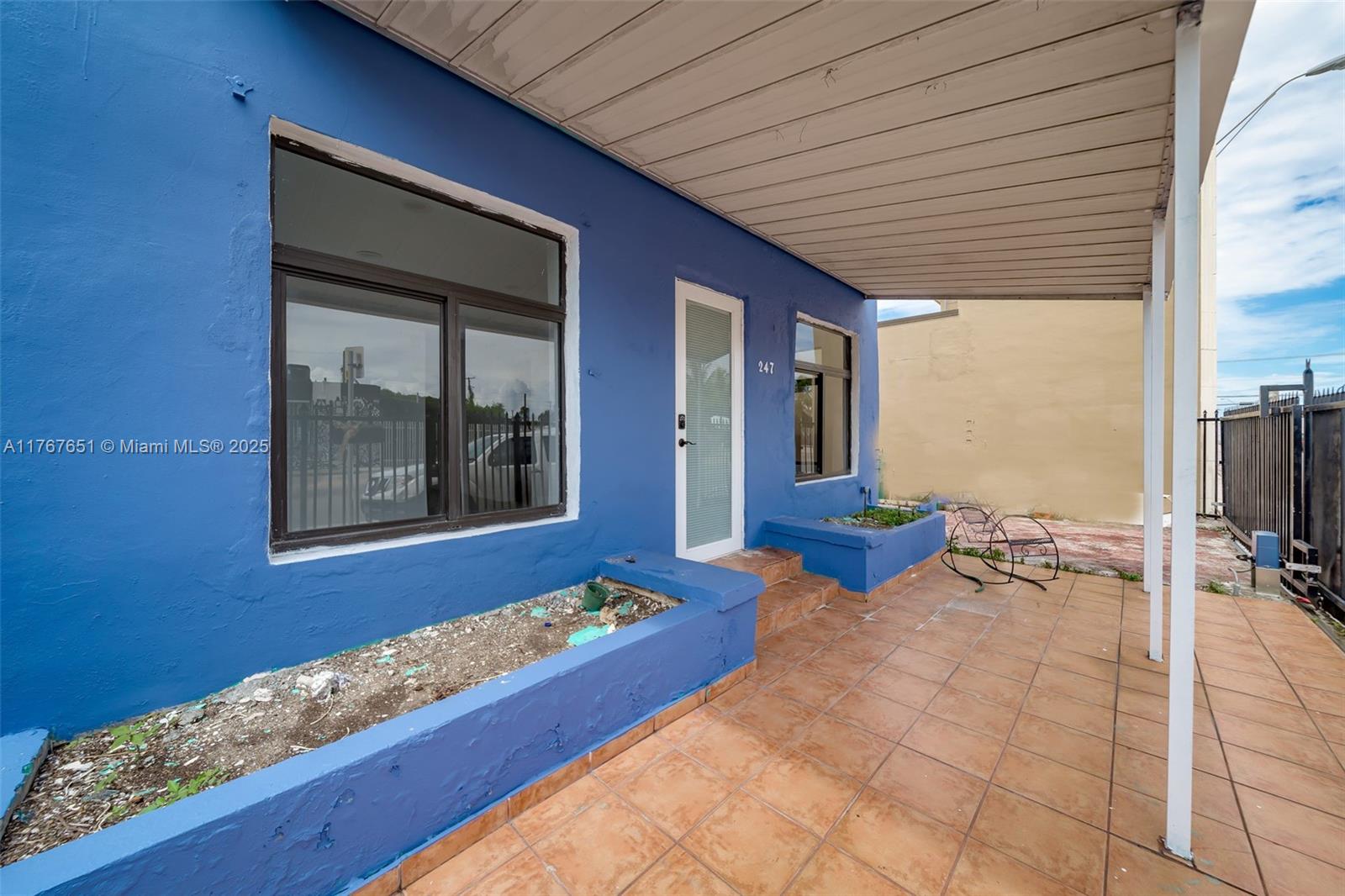 A blue exterior wall features a front door, two windows, and a tiled porch area — 247 NW 54th St, Miami FL 33127, MIAMI, FL