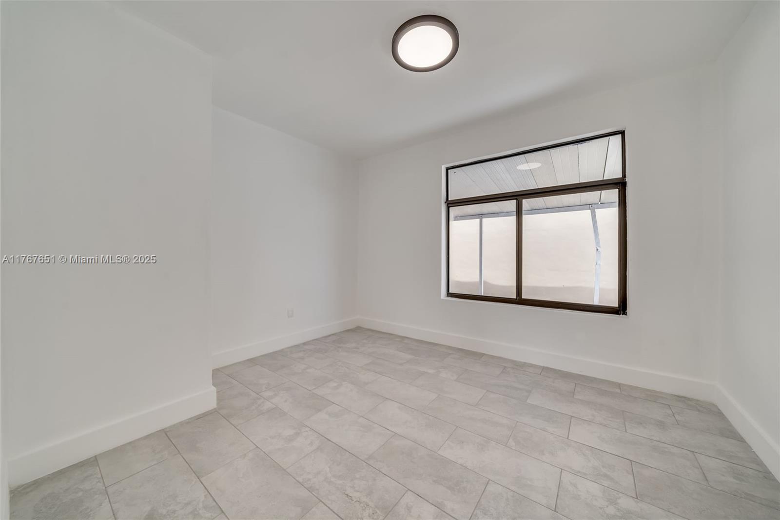 An empty room features white walls, light gray tile flooring, and a large window — 247 NW 54th St, Miami FL 33127, MIAMI, FL