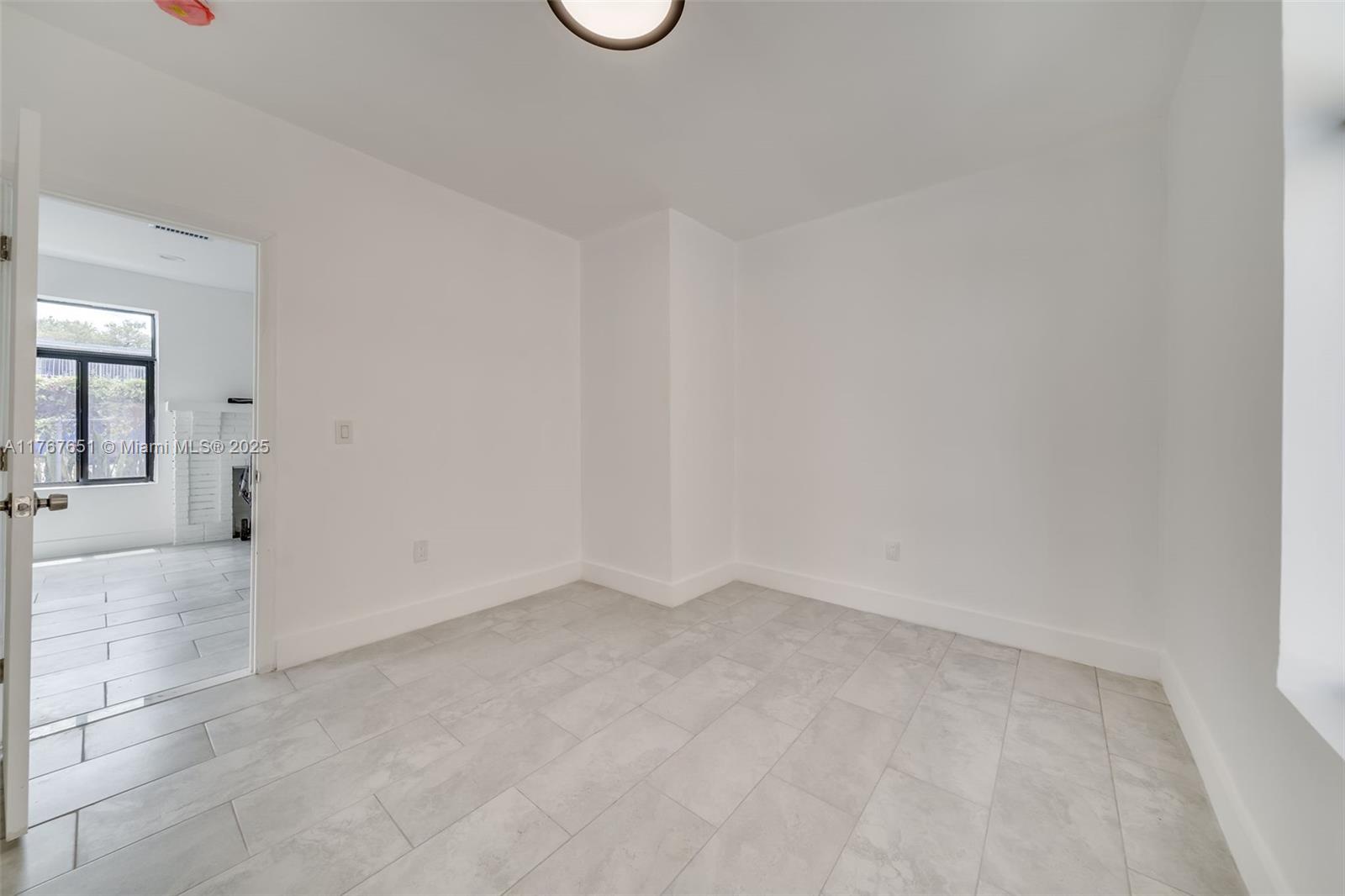 An empty room with white walls and light-colored tile flooring features a doorway to another room — 247 NW 54th St, Miami FL 33127, MIAMI, FL