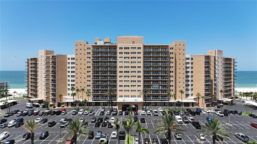 An aerial view shows a large, multi-story beachfront apartment complex with a parking lot — 880 MANDALAY AVENUE UNIT C808, CLEARWATER BEACH, FL