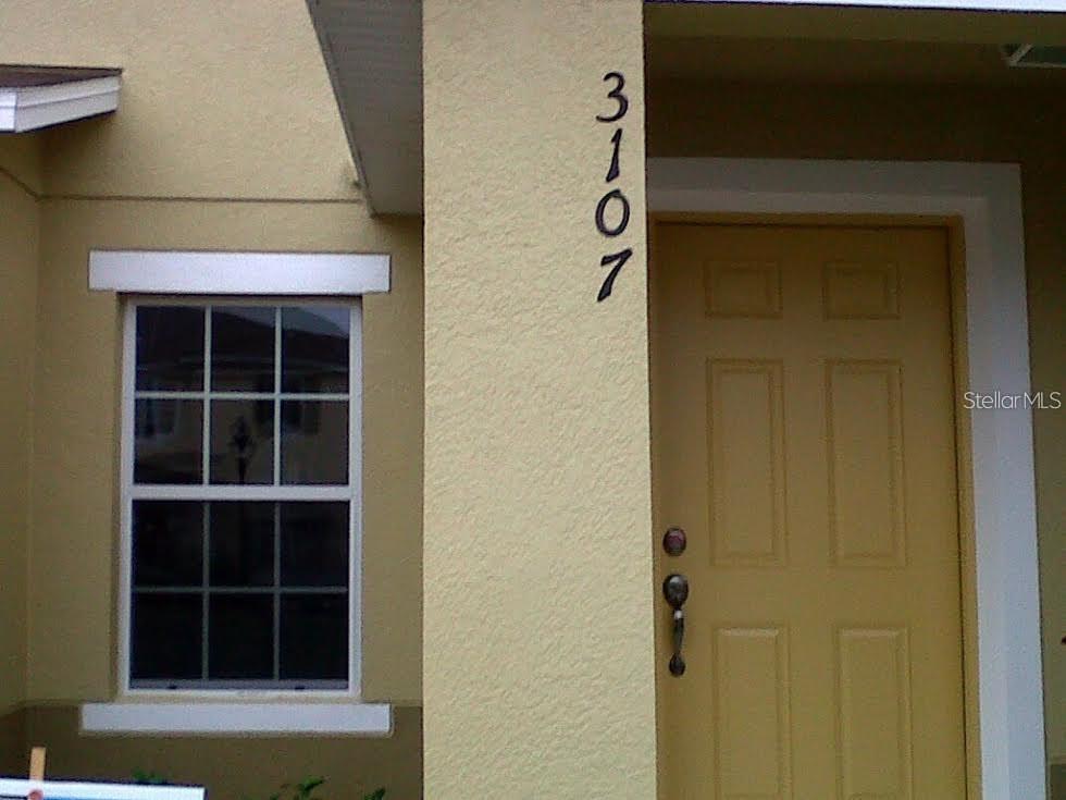A tan exterior wall features a vertical house number, a white-framed window, and a door — 3107 SEAVIEW CASTLE DRIVE, KISSIMMEE, FL