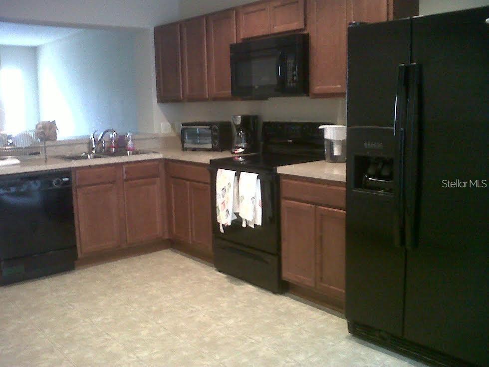 A kitchen features wood cabinets, black appliances, and light-colored tile flooring — 3107 SEAVIEW CASTLE DRIVE, KISSIMMEE, FL