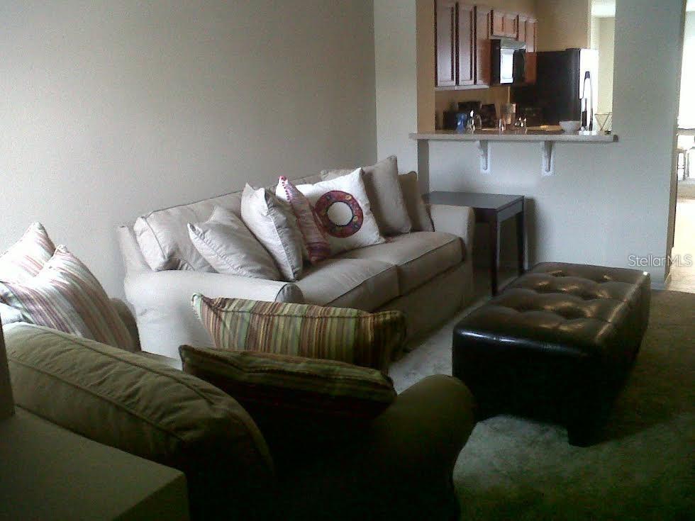 A living room features a beige sofa, a leather ottoman, and an open kitchen area — 3107 SEAVIEW CASTLE DRIVE, KISSIMMEE, FL