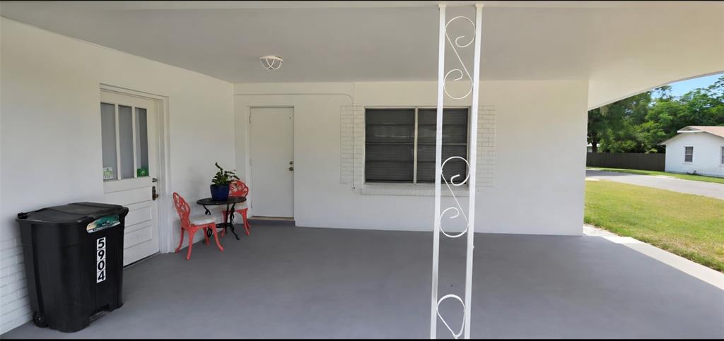 A covered concrete patio features a white door, a window, and a decorative metal support column — 5904 ELM STREET, NEW PORT RICHEY, FL