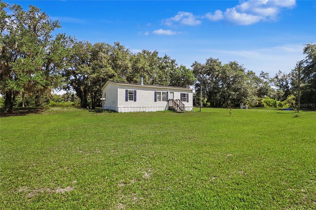 A single-story manufactured home sits on a large, grassy lot surrounded by mature trees — 5435 NE 153RD PLACE ROAD, CITRA, FL