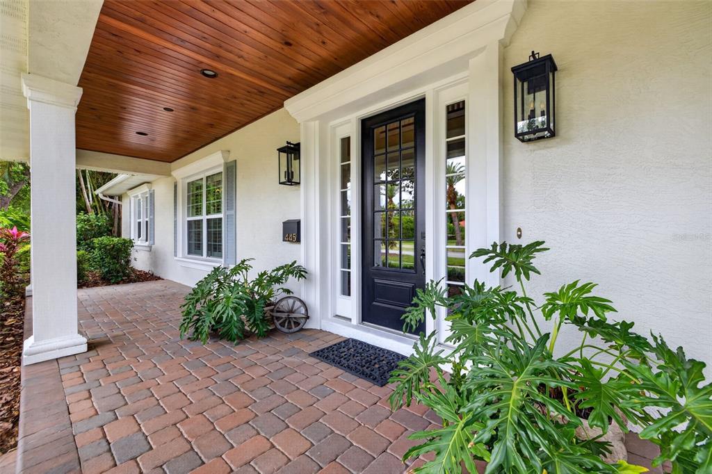 A front porch with a wood-paneled ceiling, brick pavers, and a black front door — 445 PARK AVENUE, BELLEAIR, FL