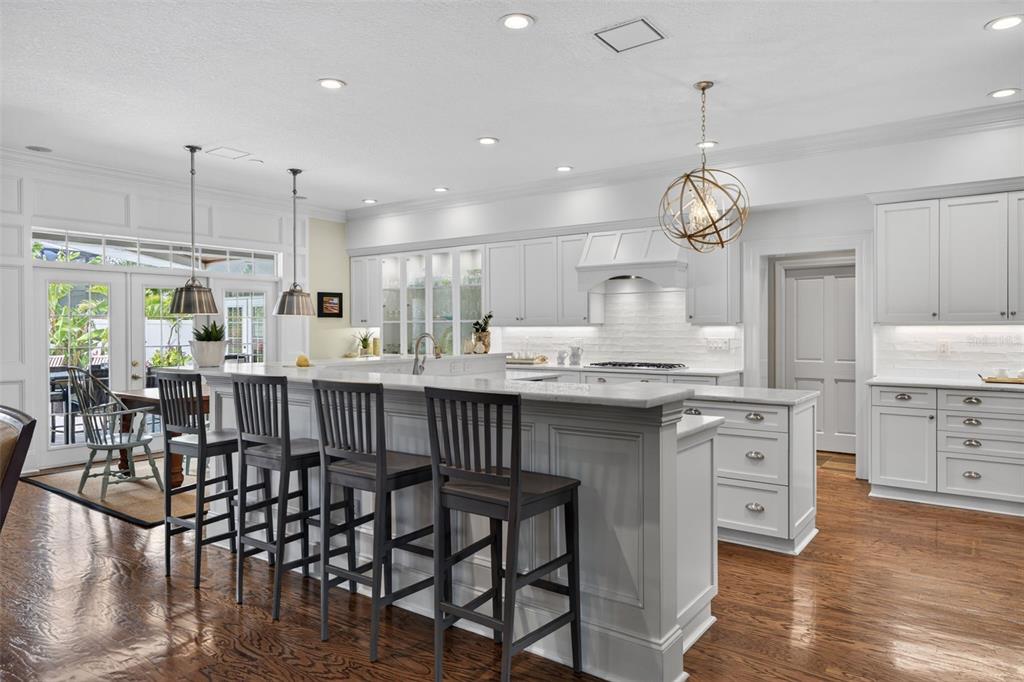 A white kitchen features a large island with dark stools and hardwood flooring — 445 PARK AVENUE, BELLEAIR, FL
