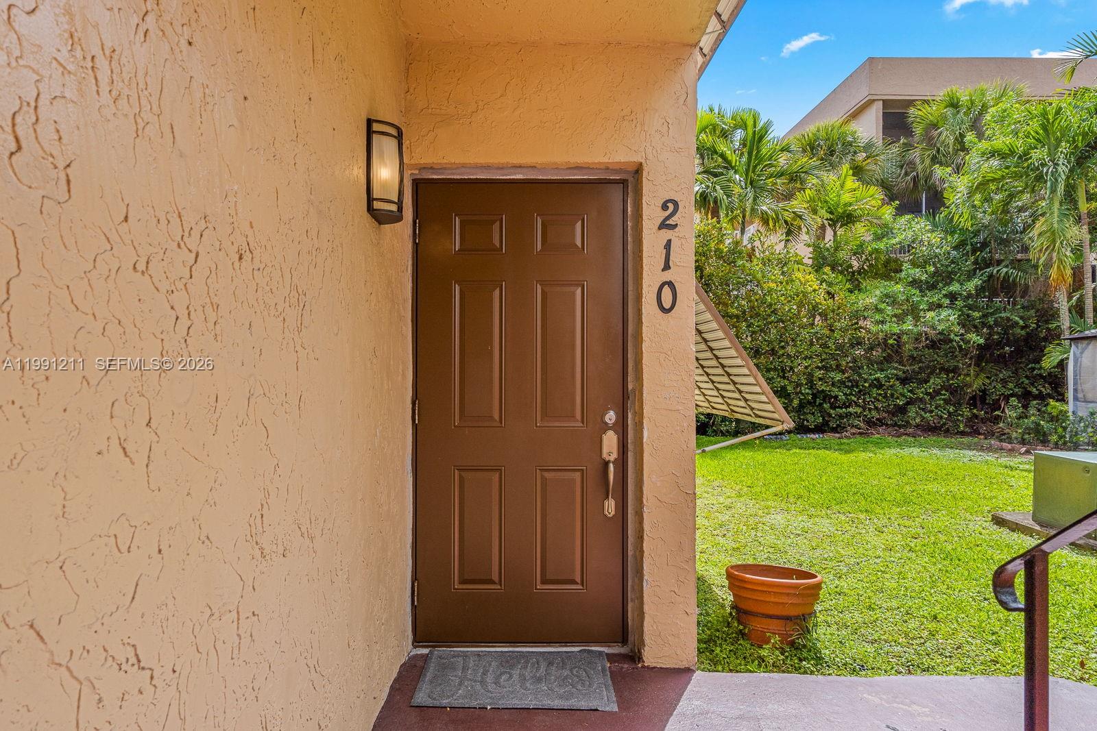 A brown front door with the number 210 is set into a beige stucco exterior wall — 6854 NW 173rd Dr # 210, Hialeah FL 33015, HIALEAH, FL