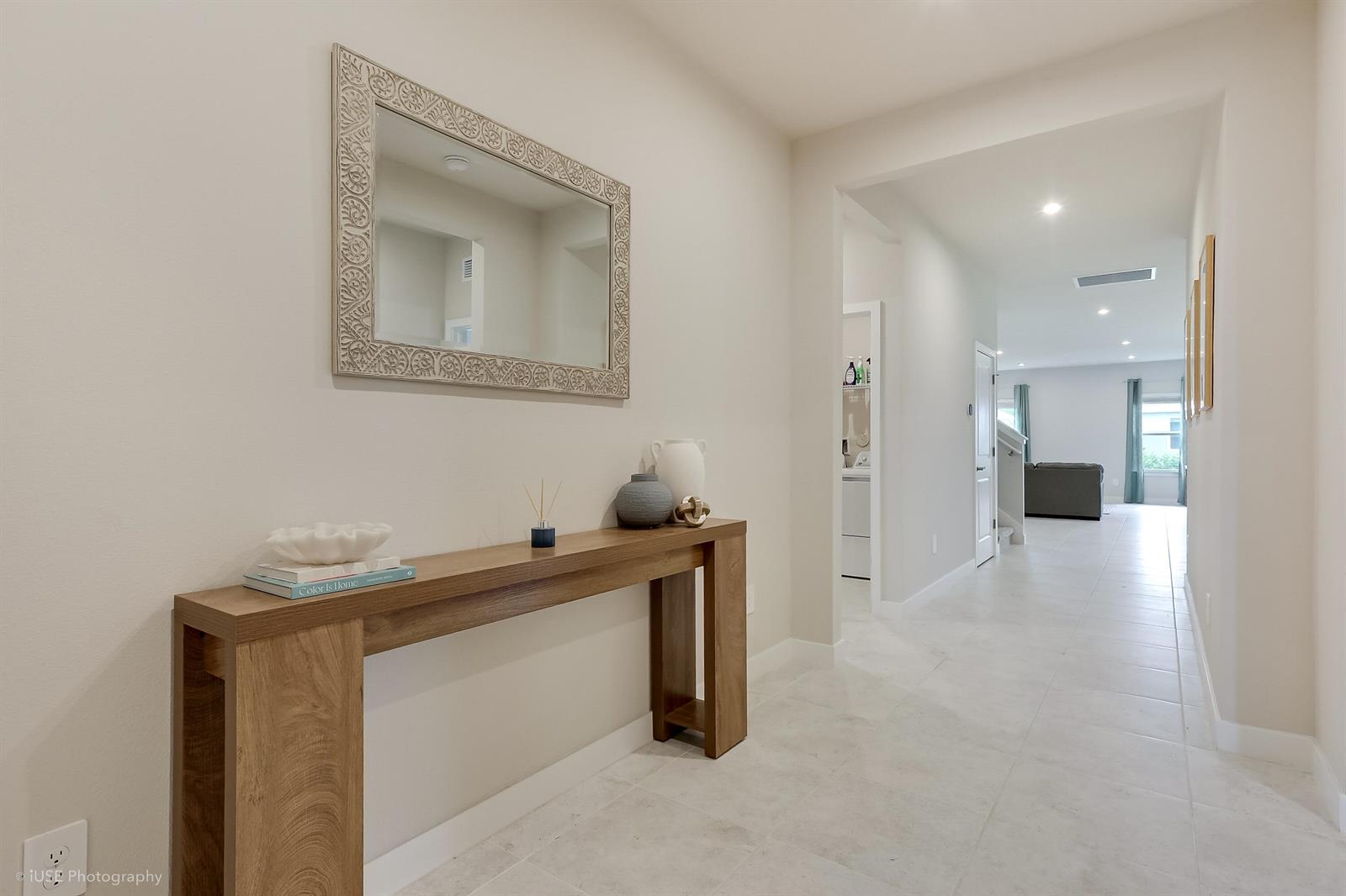 A hallway features a wooden console table, a decorative mirror, and light-colored tile flooring — 84 Jetty Lane, Sebastian FL 32958, SEBASTIAN, FL