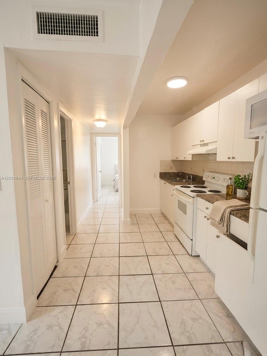 A galley kitchen with white cabinets, white appliances, and light-colored tile flooring — 2745 W Okeechobee Rd # 5, Hialeah FL 33010, HIALEAH, FL