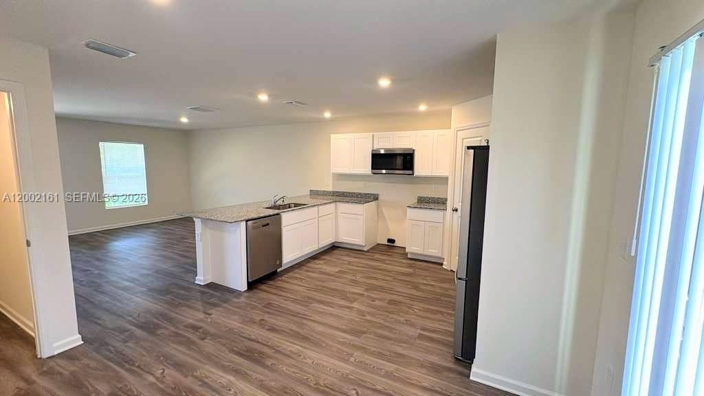 A kitchen with white cabinets, granite countertops, and wood-look flooring opens to a living area — OTHER CITY - IN THE STATE OF FLORIDA, FL