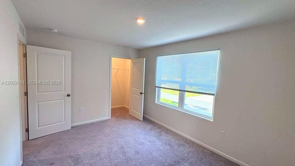 This bedroom features neutral walls, gray carpeting, a walk-in closet, and a window with blinds — OTHER CITY - IN THE STATE OF FLORIDA, FL