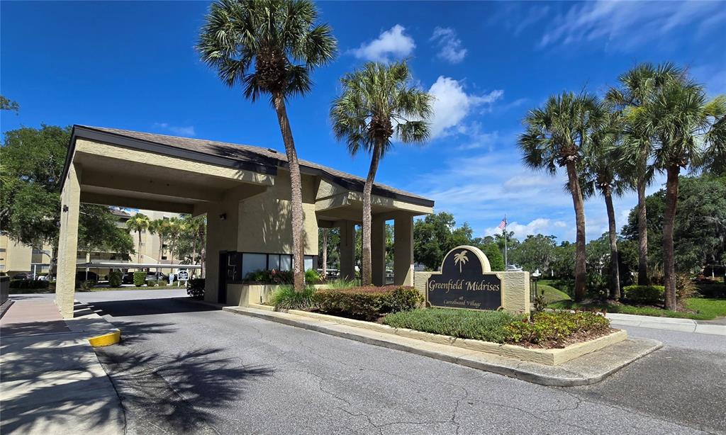 The entrance to Greenfield Midrises at Carrollwood Village features a covered gatehouse and palm trees — 13626 GREENFIELD DRIVE UNIT 201, TAMPA, FL