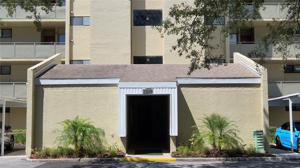 The exterior of a multi-story apartment building features a covered entrance with a shingled roof — 13626 GREENFIELD DRIVE UNIT 201, TAMPA, FL
