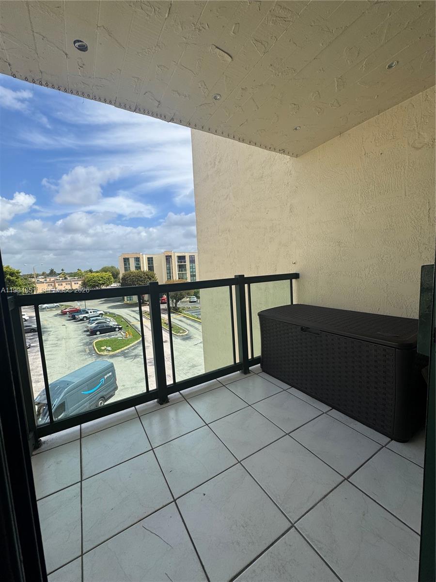 A balcony with white tile flooring, a black storage bin, and a glass-paneled railing — 2055 SW 122nd Ave # 403, Miami FL 33175, MIAMI, FL