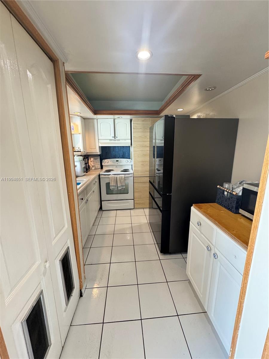 A galley-style kitchen features white cabinets, a black refrigerator, and white tiled flooring — 2055 SW 122nd Ave # 403, Miami FL 33175, MIAMI, FL