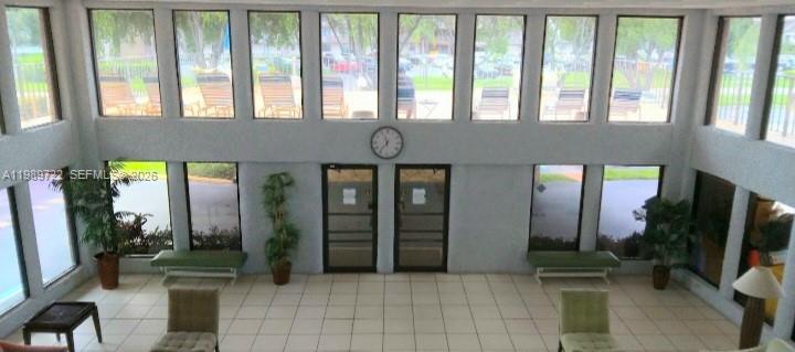 A high-ceilinged lobby features large windows, tiled floors, two glass doors, and a wall clock — 9273 SW 8th St # 220, Boca Raton FL 33428, BOCA RATON, FL
