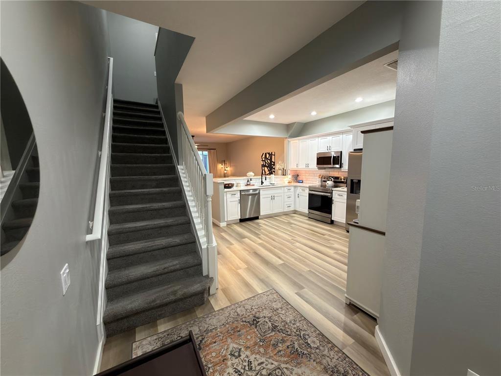 A staircase with dark carpet leads upward next to a kitchen with white cabinets — 26605 CHIMNEY SPIRE LANE, WESLEY CHAPEL, FL
