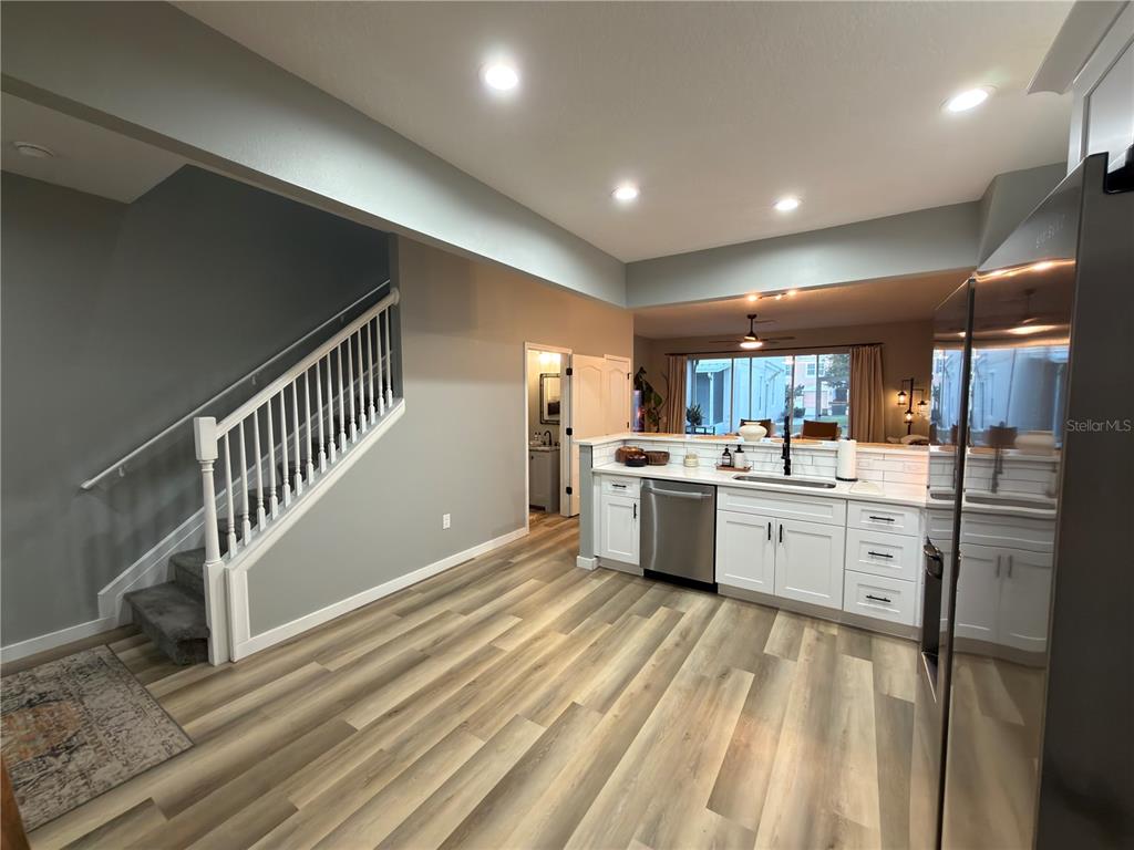 A kitchen with white cabinets and stainless steel appliances sits beside a carpeted staircase — 26605 CHIMNEY SPIRE LANE, WESLEY CHAPEL, FL