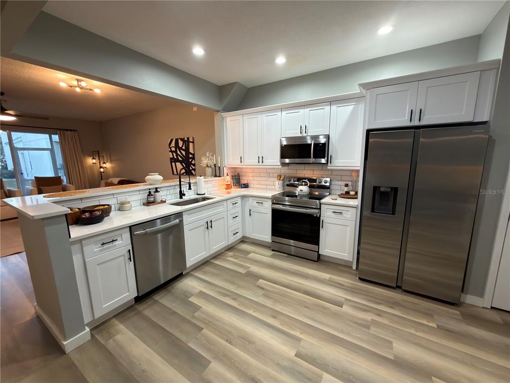 A kitchen features white cabinets, stainless steel appliances, and light wood-look flooring — 26605 CHIMNEY SPIRE LANE, WESLEY CHAPEL, FL