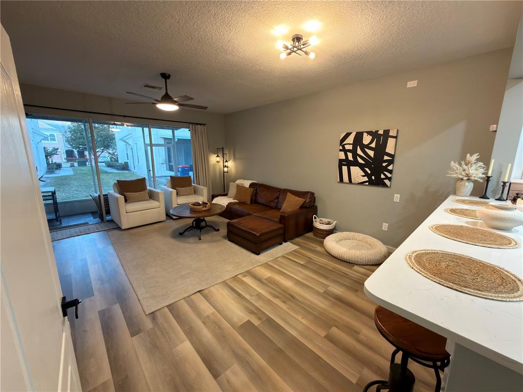 A living room with wood-look flooring, a leather sectional, two armchairs, and a kitchen island — 26605 CHIMNEY SPIRE LANE, WESLEY CHAPEL, FL