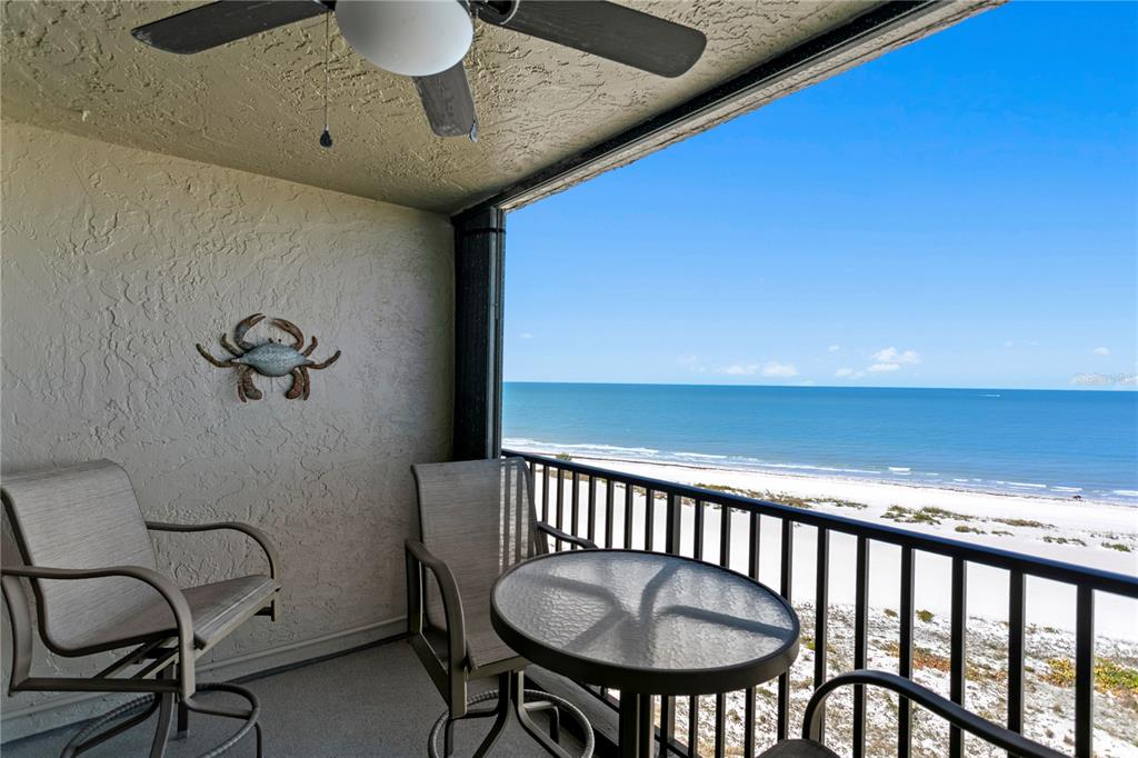 A balcony with outdoor furniture and a crab wall decoration overlooks a sandy beach — 1290 GULF BOULEVARD UNIT 1002, CLEARWATER, FL