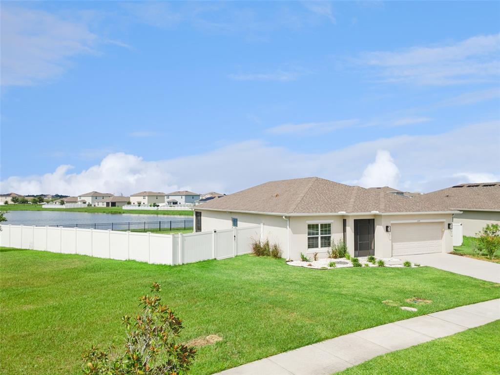A single-story house with a beige exterior, a two-car garage, and a white vinyl fence — 309 CITRINE LOOP, KISSIMMEE, FL