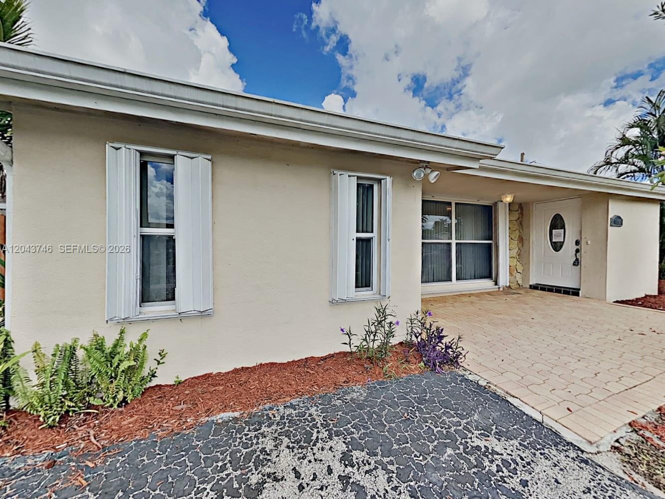 The exterior of a single-story house features beige stucco walls, white shutters, and a paved walkway — PEMBROKE PINES, FL