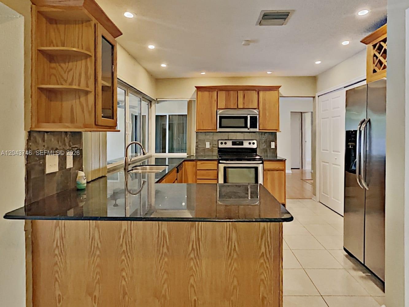 A kitchen features wood cabinets, dark granite countertops, stainless steel appliances, and tile flooring — PEMBROKE PINES, FL