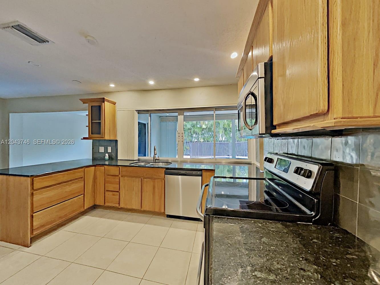 A kitchen features light wood cabinets, dark countertops, a stainless steel dishwasher, and a window — PEMBROKE PINES, FL