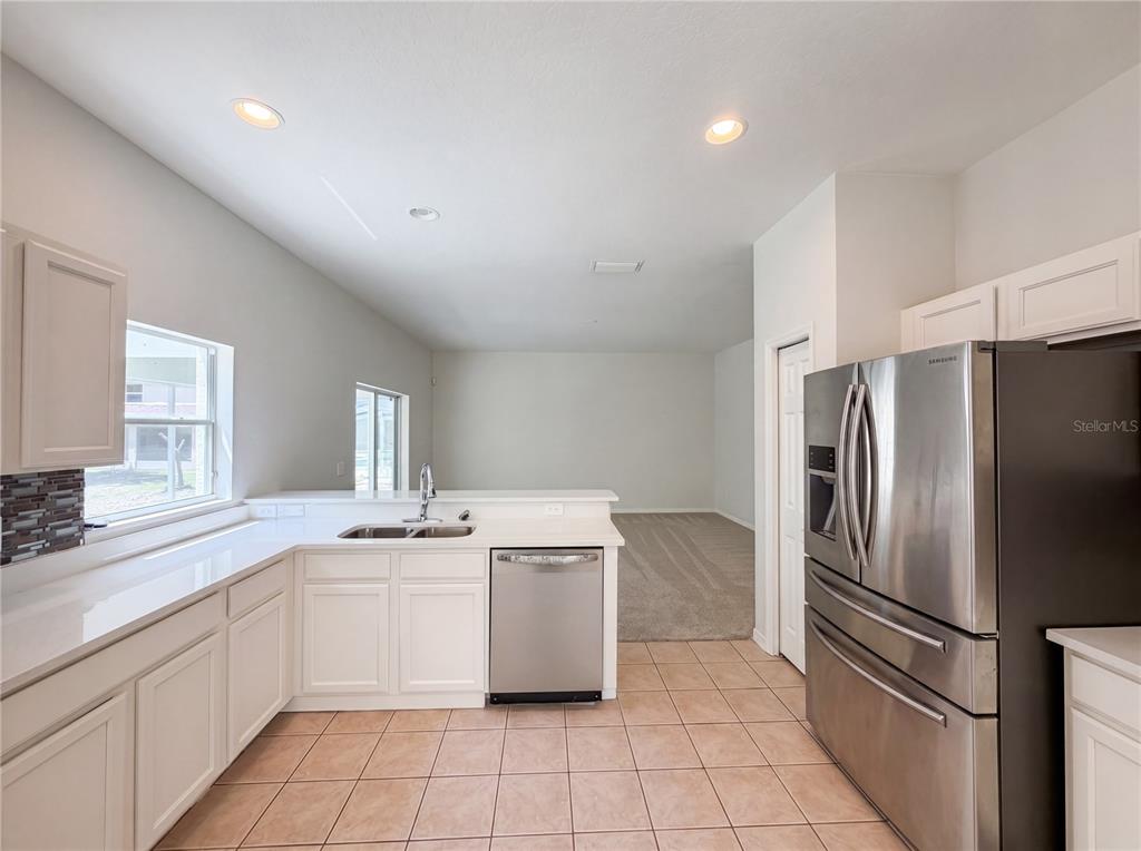 A kitchen with white cabinets, stainless steel appliances, and tile flooring overlooks an adjacent carpeted room — 8116 RIVER MONT WAY, TEMPLE TERRACE, FL