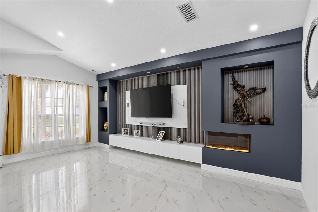 A modern living room features a large wall-mounted television, a fireplace, and white marble flooring — 738 HACIENDA CIRCLE, KISSIMMEE, FL