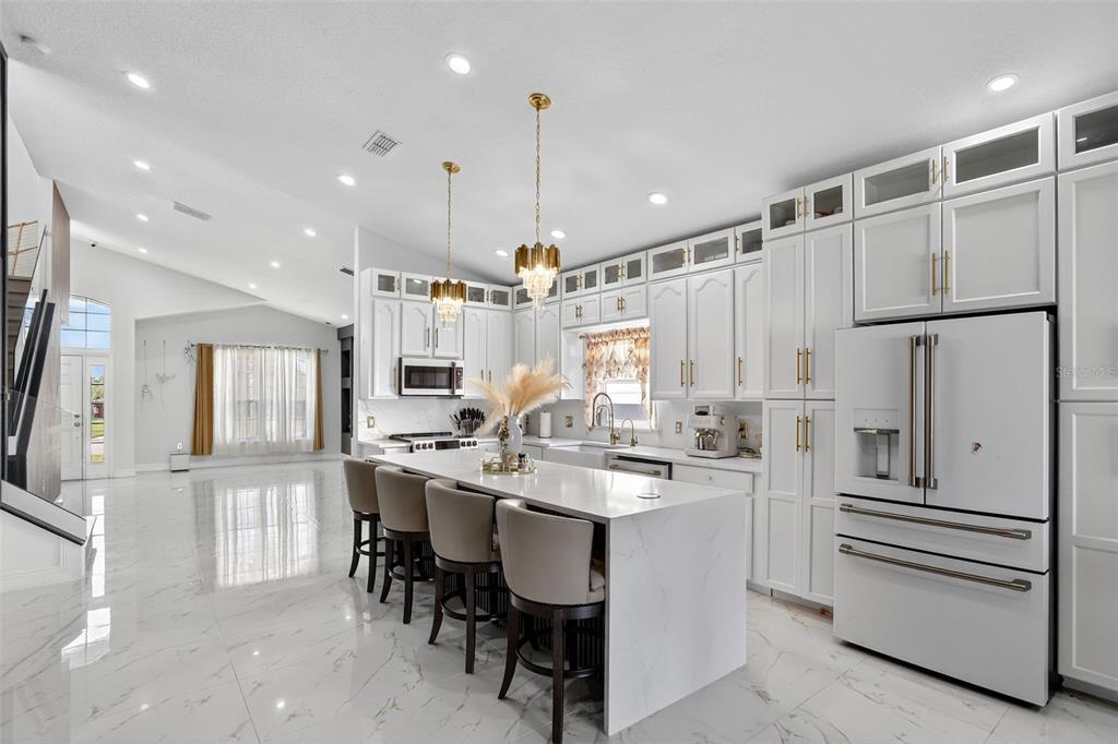 A modern white kitchen features a marble-topped island, gold pendant lights, and glossy tile floors — 738 HACIENDA CIRCLE, KISSIMMEE, FL