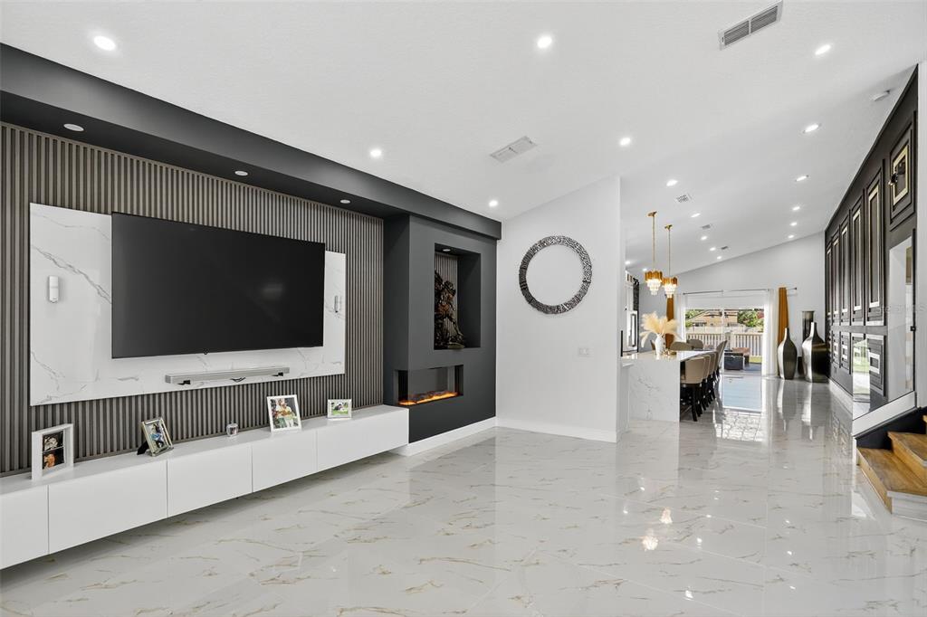 A modern living room features a marble-accented media wall, fireplace, and polished tile flooring — 738 HACIENDA CIRCLE, KISSIMMEE, FL