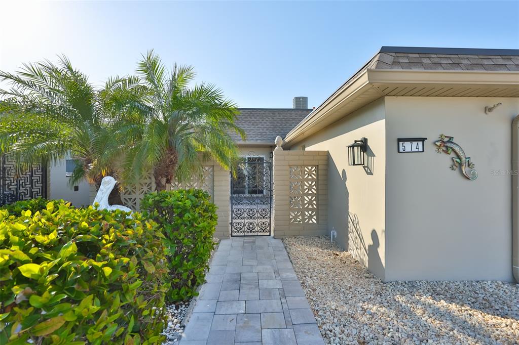 A paved walkway leads to a gated courtyard entrance of a house with beige walls — 574 BOCA CIEGA POINT BOULEVARD N UNIT 2205, ST PETERSBURG, FL