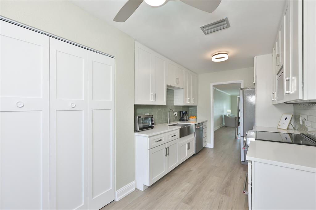 A galley kitchen features white cabinets, light wood-look flooring, and a stainless steel farmhouse sink — 574 BOCA CIEGA POINT BOULEVARD N UNIT 2205, ST PETERSBURG, FL