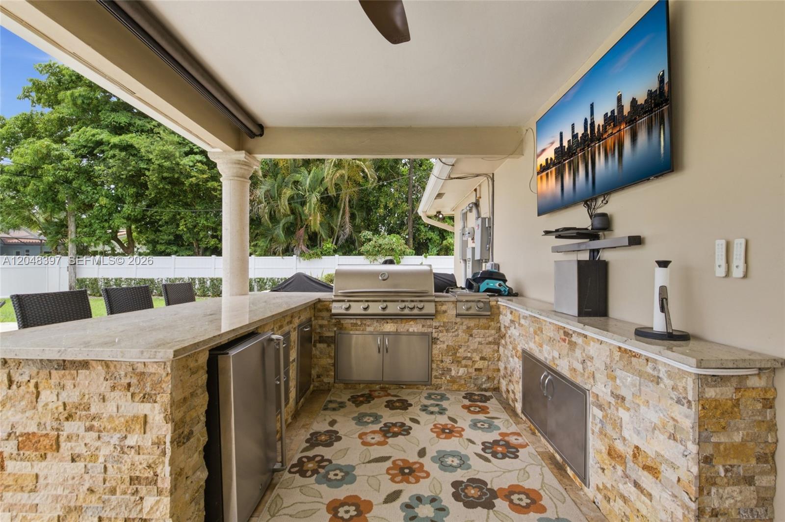 An outdoor kitchen features a stone-clad bar, stainless steel appliances, and a wall-mounted television — 621 NW 74th Ave, Plantation FL 33317, PLANTATION, FL