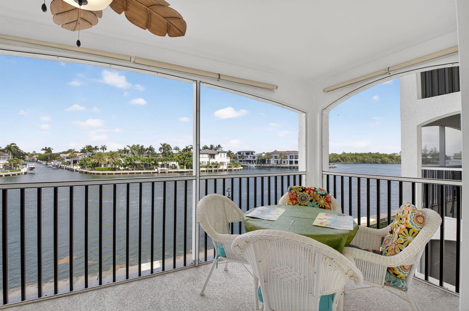 A screened-in balcony features white wicker furniture and a view of a waterfront residential area — 2871 N Ocean Boulevard # R254, Boca Raton FL 33431, BOCA RATON, FL