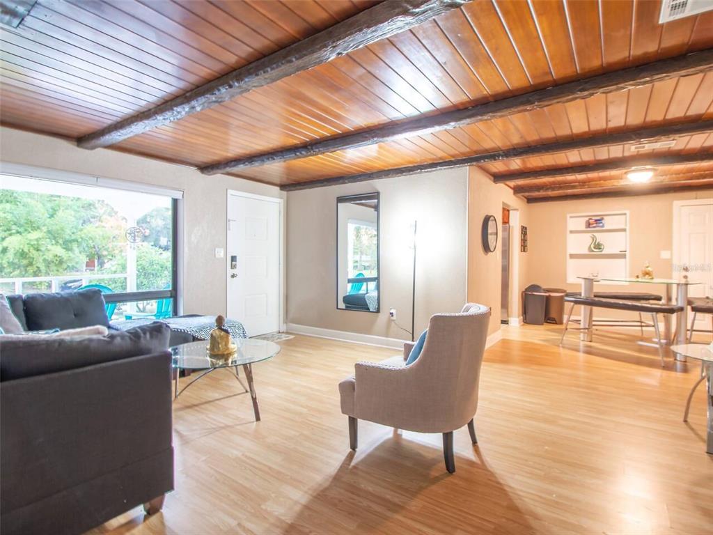 A living room with wood-paneled ceilings, exposed beams, light wood flooring, and a dining area — 1245 CATALPA LN UNIT 1, ORLANDO, FL