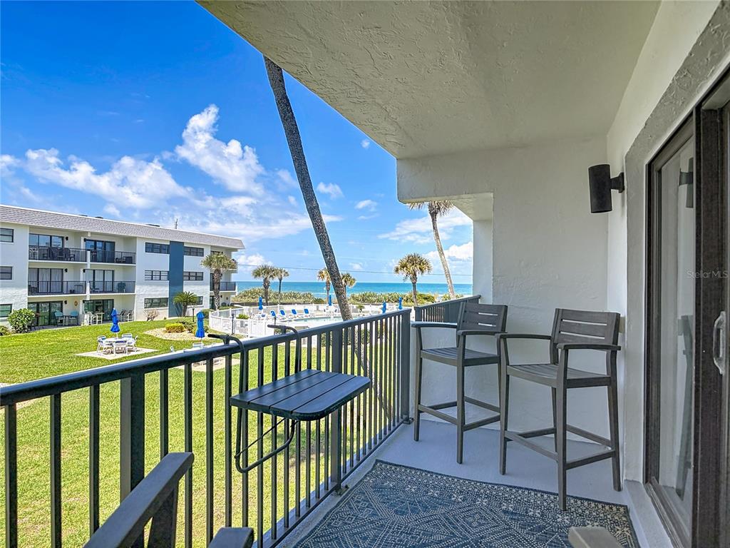A balcony with a metal railing, outdoor chairs, and a table overlooking a pool area — 2100 OCEAN SHORE BOULEVARD UNIT 2070, ORMOND BEACH, FL