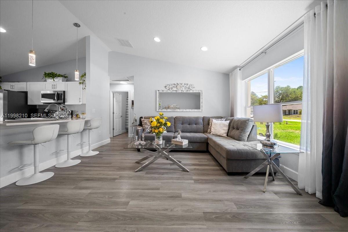 A living room with a gray sectional sofa, glass coffee table, and adjacent kitchen area — 13789 102nd Pl, Ocala FL 34432, OCALA, FL