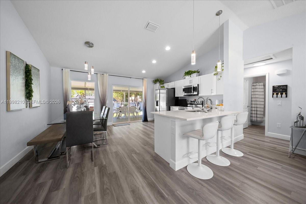 This open-concept kitchen features white cabinetry, a quartz island with bar seating, and wood-look flooring — 13789 102nd Pl, Ocala FL 34432, OCALA, FL