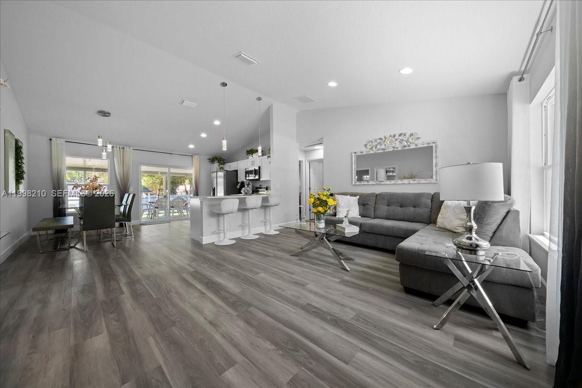 A bright open-concept living and dining area features gray wood-look flooring and white cabinetry — 13789 102nd Pl, Ocala FL 34432, OCALA, FL