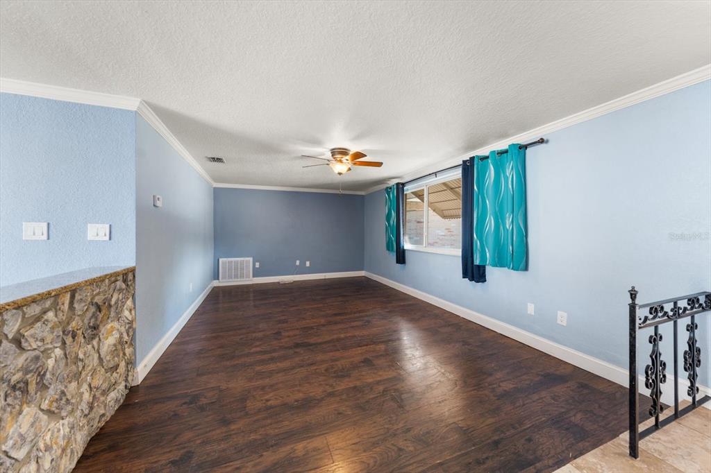 An empty room with blue walls, dark wood flooring, a ceiling fan, and stone accents — 4025 SAIL DRIVE, NEW PORT RICHEY, FL
